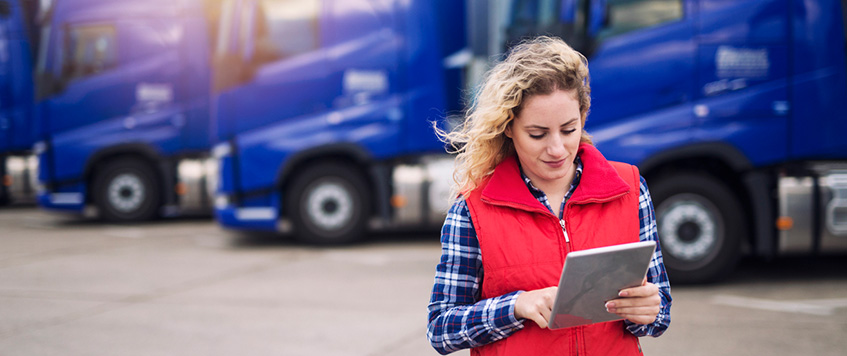 Woman standing with tablet in front of trucks, trucking industry concept